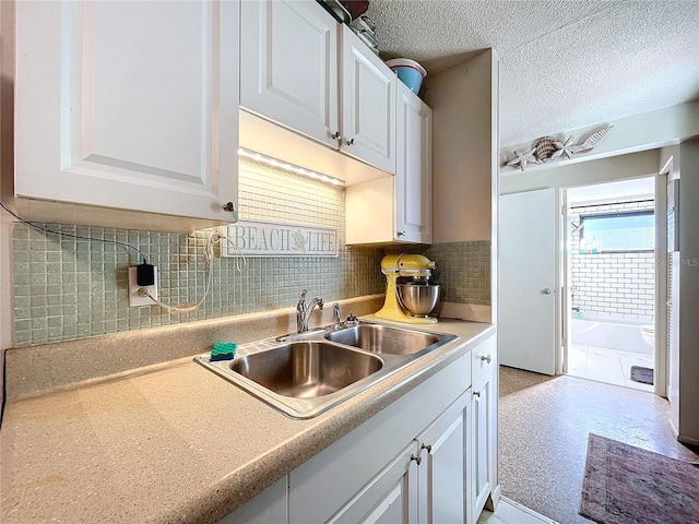 kitchen with white cabinets, a sink, light countertops, a textured ceiling, and backsplash