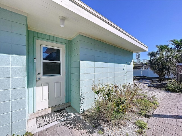 view of exterior entry featuring concrete block siding and fence