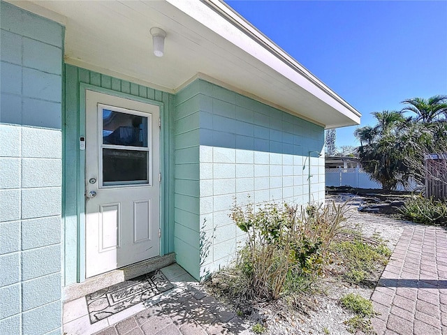 view of exterior entry featuring concrete block siding and fence