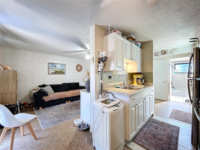 kitchen with light countertops, backsplash, a ceiling fan, freestanding refrigerator, and a sink