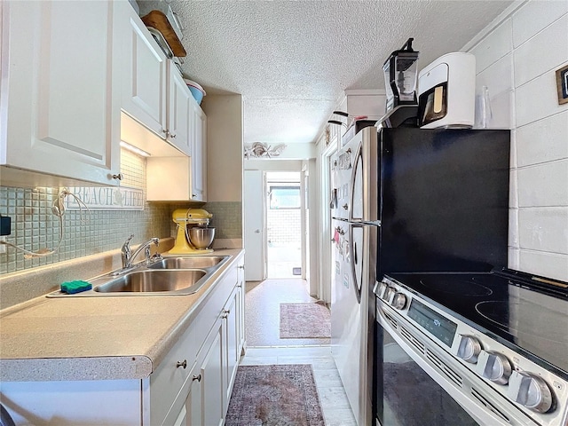 kitchen with a sink, a textured ceiling, stainless steel range with electric stovetop, white cabinetry, and backsplash