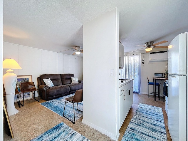 living room featuring a ceiling fan, tile walls, a textured ceiling, and baseboards