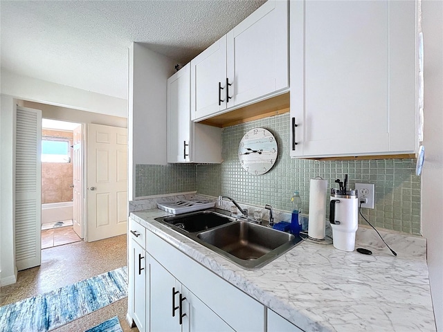 kitchen featuring a textured ceiling, white cabinetry, light countertops, and a sink