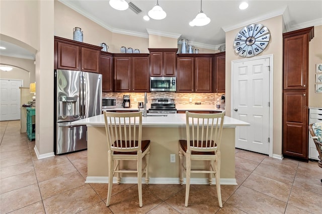 kitchen featuring stainless steel appliances, a breakfast bar area, a kitchen island with sink, and decorative light fixtures