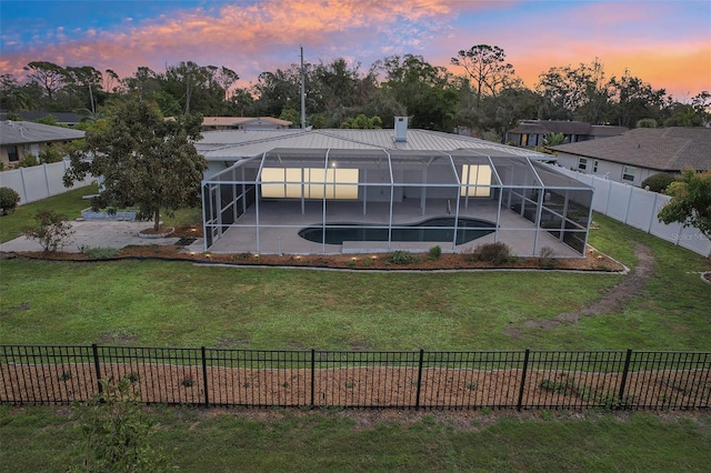 back house at dusk featuring a yard, a fenced in pool, a patio area, and glass enclosure