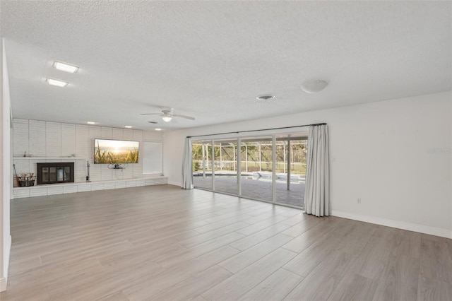 unfurnished living room with a brick fireplace, light hardwood / wood-style floors, a textured ceiling, and ceiling fan