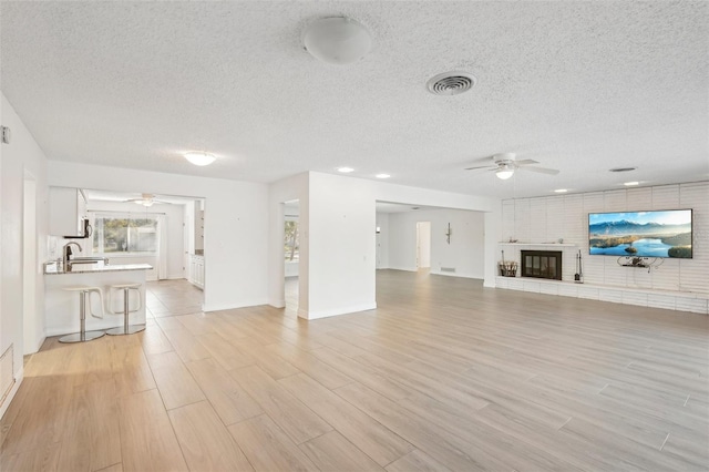 unfurnished living room with ceiling fan, a brick fireplace, sink, and light hardwood / wood-style floors