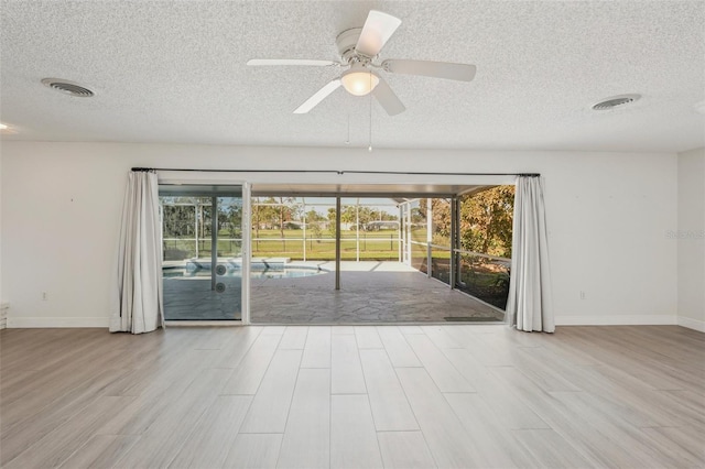 empty room with ceiling fan, a healthy amount of sunlight, light hardwood / wood-style floors, and a textured ceiling