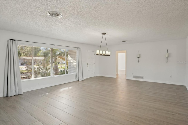 spare room featuring hardwood / wood-style flooring, a chandelier, and a textured ceiling