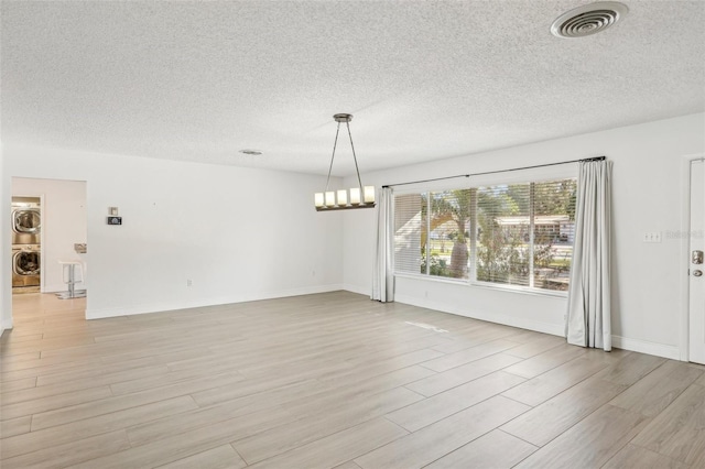 empty room featuring an inviting chandelier, stacked washer / drying machine, light hardwood / wood-style flooring, and a textured ceiling