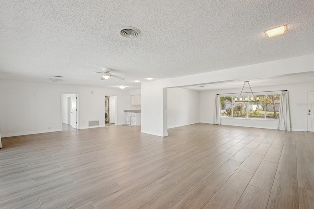 unfurnished living room featuring ceiling fan with notable chandelier, a textured ceiling, and light wood-type flooring