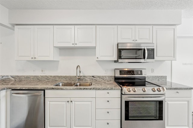 kitchen featuring appliances with stainless steel finishes, white cabinetry, sink, light stone countertops, and a textured ceiling