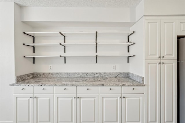 interior space featuring a textured ceiling, white cabinets, and light stone counters