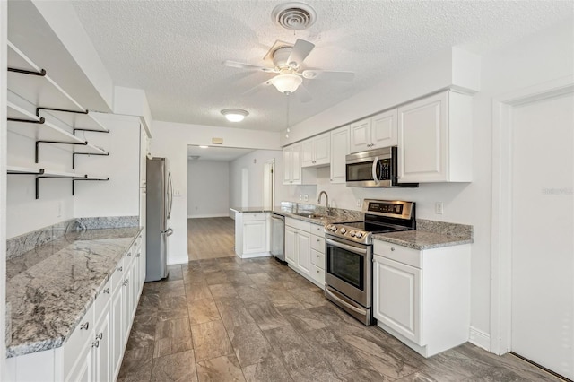 kitchen featuring appliances with stainless steel finishes, sink, white cabinets, ceiling fan, and light stone countertops