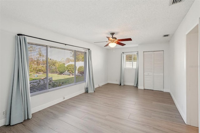 empty room featuring ceiling fan, light hardwood / wood-style floors, and a textured ceiling