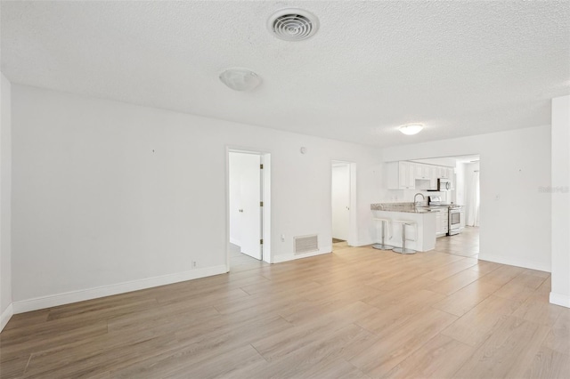 unfurnished living room with light hardwood / wood-style flooring and a textured ceiling