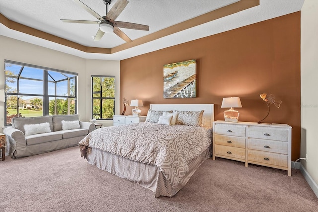 carpeted bedroom featuring a raised ceiling, ceiling fan, a textured ceiling, and baseboards