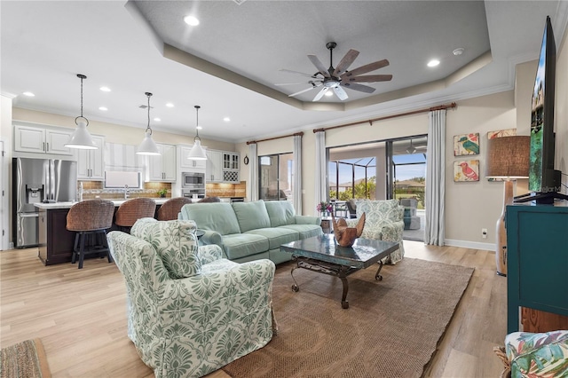 living room featuring baseboards, ceiling fan, ornamental molding, a tray ceiling, and light wood-style floors