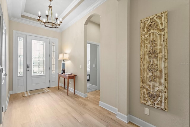 entryway featuring arched walkways, a tray ceiling, light wood-style flooring, ornamental molding, and baseboards