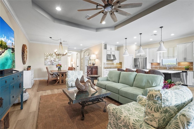 living area with a raised ceiling, crown molding, and light wood finished floors