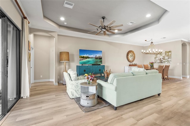 living room featuring arched walkways, visible vents, light wood finished floors, and a tray ceiling