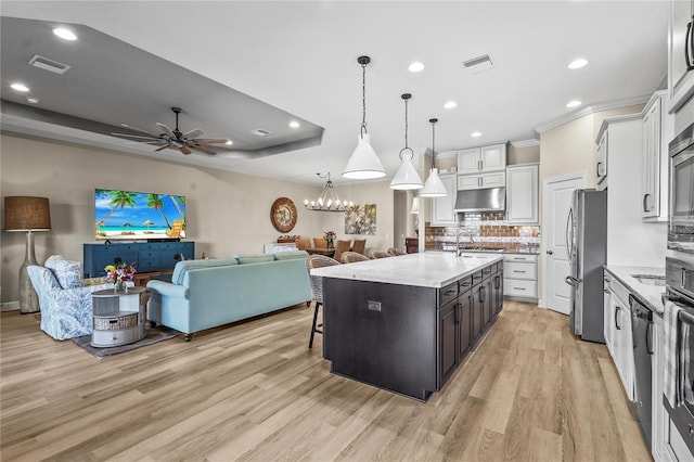 kitchen featuring open floor plan, visible vents, a raised ceiling, and under cabinet range hood