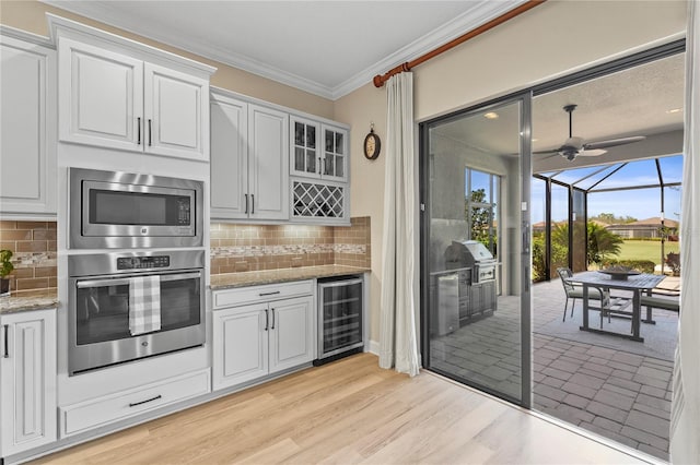 kitchen with crown molding, stainless steel microwave, a sunroom, light wood-type flooring, and beverage cooler