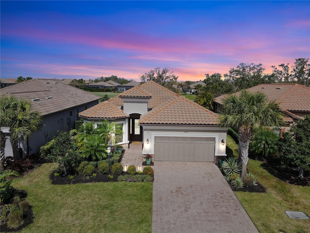 mediterranean / spanish-style home featuring a tiled roof, an attached garage, decorative driveway, a front yard, and stucco siding