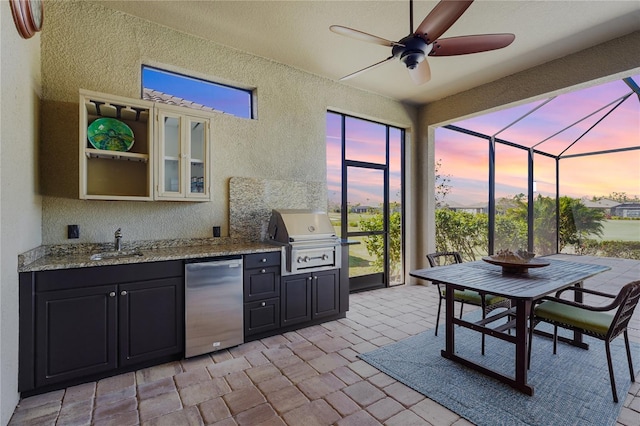 view of patio with an outdoor kitchen, a lanai, a sink, a ceiling fan, and a grill