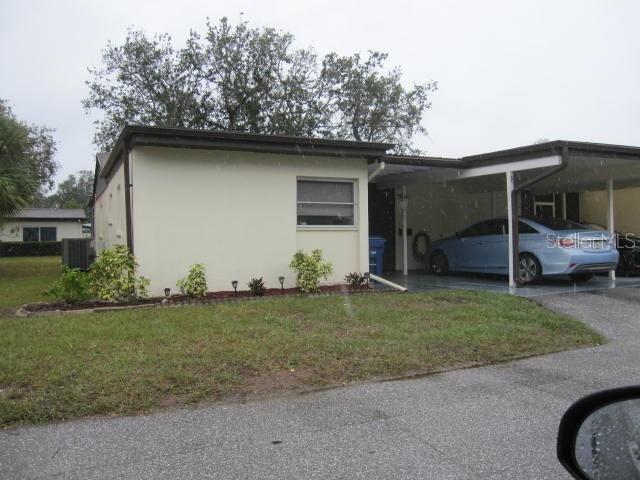 view of side of property with a lawn, aphalt driveway, central air condition unit, a carport, and stucco siding