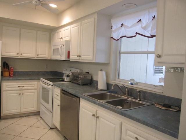 kitchen featuring dark countertops, white appliances, white cabinets, and a sink