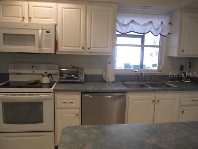 kitchen with white appliances, a toaster, dark stone countertops, white cabinetry, and a sink