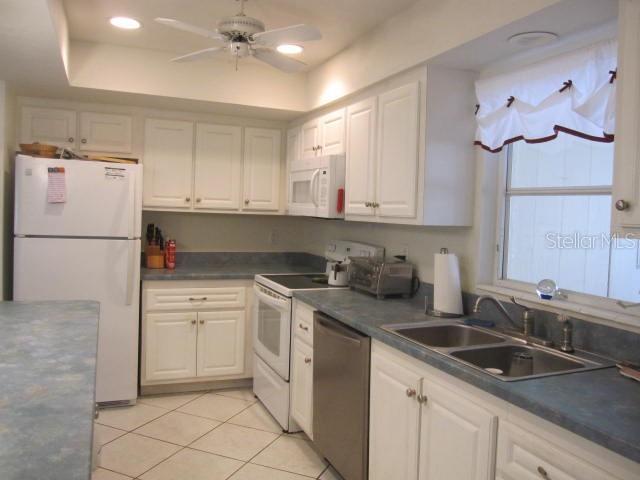 kitchen featuring white appliances, a ceiling fan, dark countertops, white cabinetry, and a sink