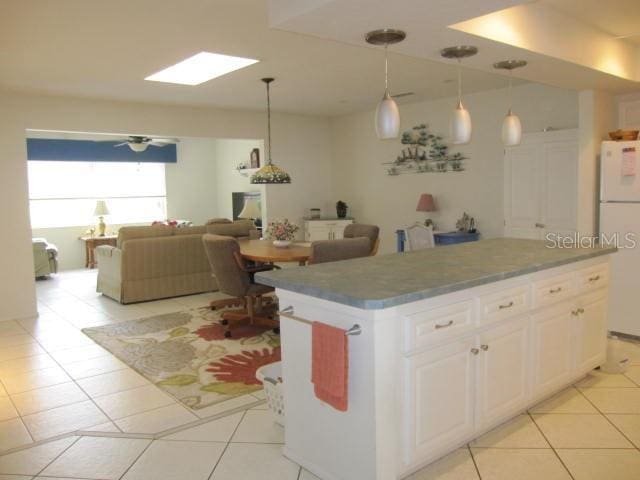 kitchen with a kitchen island, open floor plan, freestanding refrigerator, hanging light fixtures, and white cabinetry