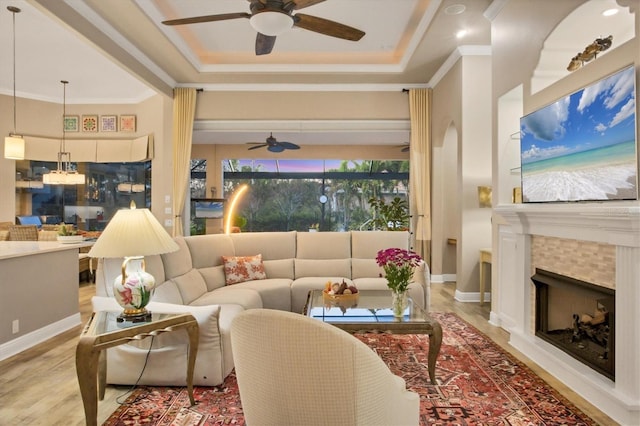 living room with crown molding, ceiling fan, light wood-type flooring, and a tray ceiling