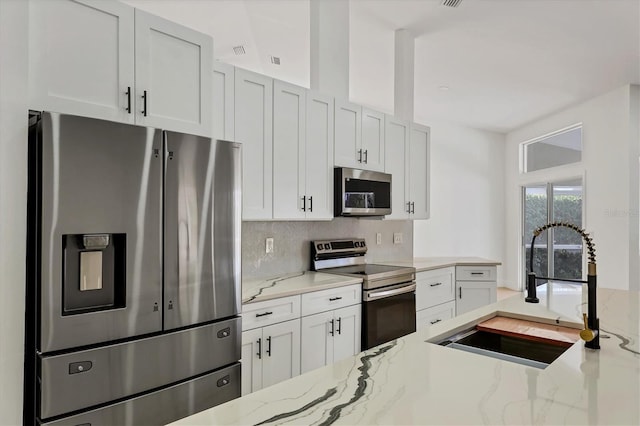 kitchen with white cabinetry, stainless steel appliances, light stone countertops, and sink