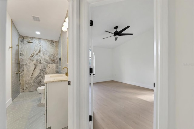 bathroom with tile walls, vanity, walk in shower, ceiling fan, and toilet