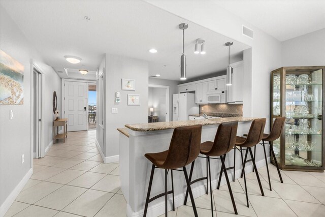 kitchen featuring white appliances, tasteful backsplash, white cabinets, light stone counters, and a peninsula