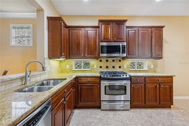 kitchen featuring decorative backsplash, appliances with stainless steel finishes, a sink, light stone countertops, and baseboards