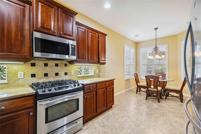 kitchen with appliances with stainless steel finishes, decorative light fixtures, light stone countertops, a chandelier, and backsplash