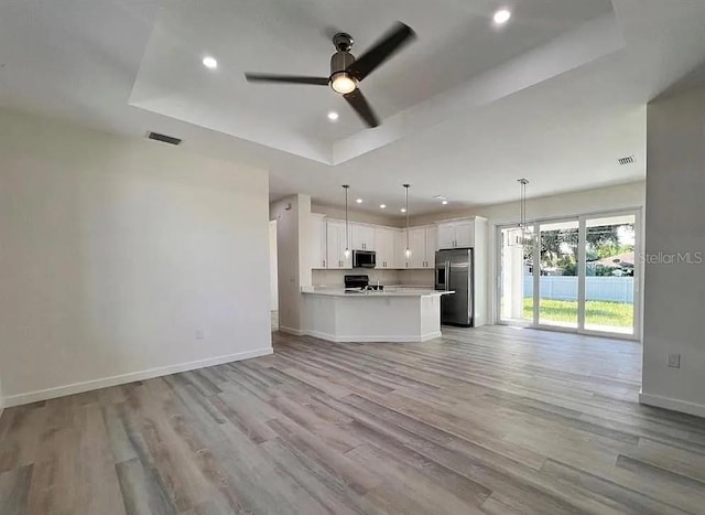 kitchen with light wood-type flooring, appliances with stainless steel finishes, a raised ceiling, pendant lighting, and white cabinets