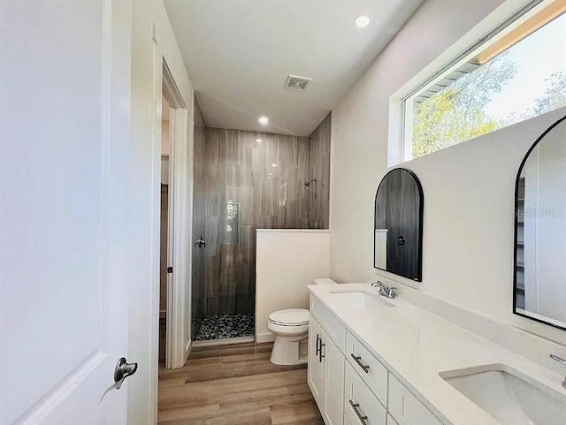 bathroom featuring hardwood / wood-style flooring, vanity, a tile shower, and toilet