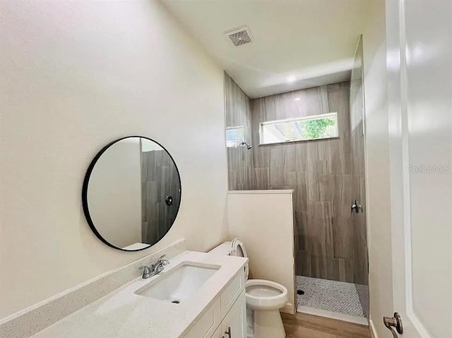 bathroom featuring vanity, hardwood / wood-style flooring, toilet, and tiled shower