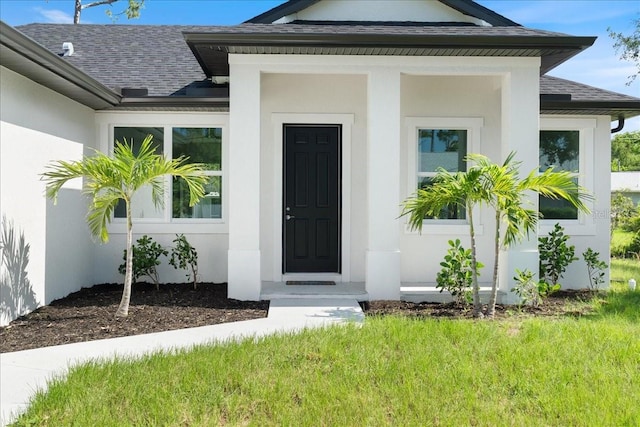 18290 Grace Ave, Port Charlotte, FL 33948 - property entrance with roof with shingles, stucco siding, and a yard