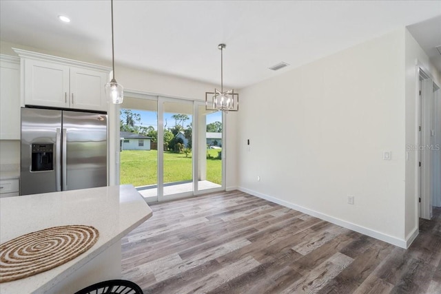 18290 Grace Ave, Port Charlotte, FL 33948 - kitchen with stainless steel refrigerator with ice dispenser, wood finished floors, white cabinets, a chandelier, and pendant lighting