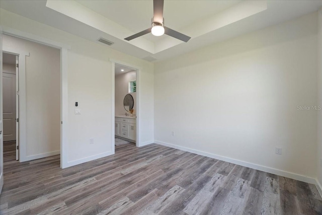 18290 Grace Ave, Port Charlotte, FL 33948 - unfurnished bedroom with wood finished floors, a tray ceiling, ensuite bath, and ceiling fan
