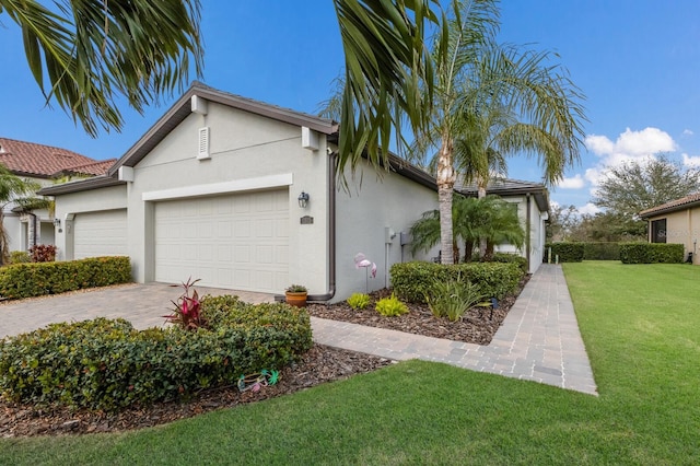 view of side of property featuring decorative driveway, an attached garage, a yard, and stucco siding