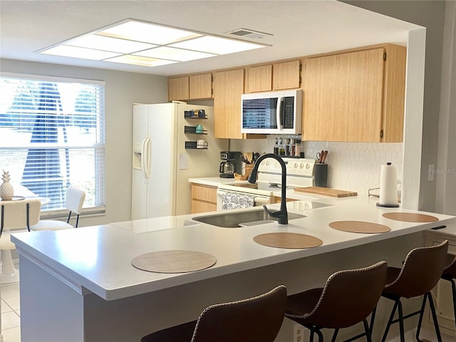 kitchen with a kitchen breakfast bar, white appliances, light brown cabinets, sink, and kitchen peninsula