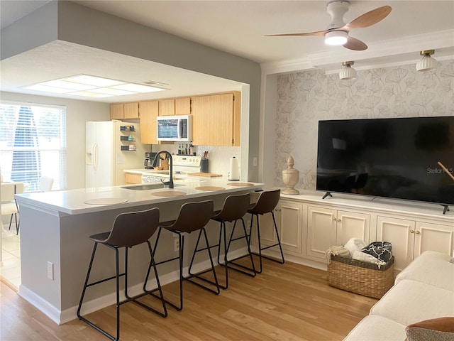 kitchen with kitchen peninsula, light hardwood / wood-style flooring, white appliances, a kitchen bar, and light brown cabinets