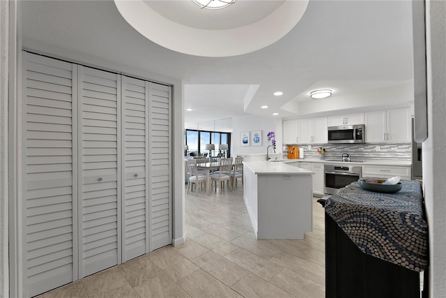 kitchen with sink, appliances with stainless steel finishes, a kitchen island with sink, white cabinets, and a raised ceiling